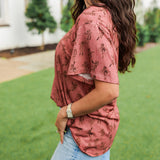 Woman with dark hair standing in a side profile position wearing the Basic Tee in a lifestyle scene. The focal point of this image is the side profile of tee with graphics. The model paired this top with light-wash denim jeans.