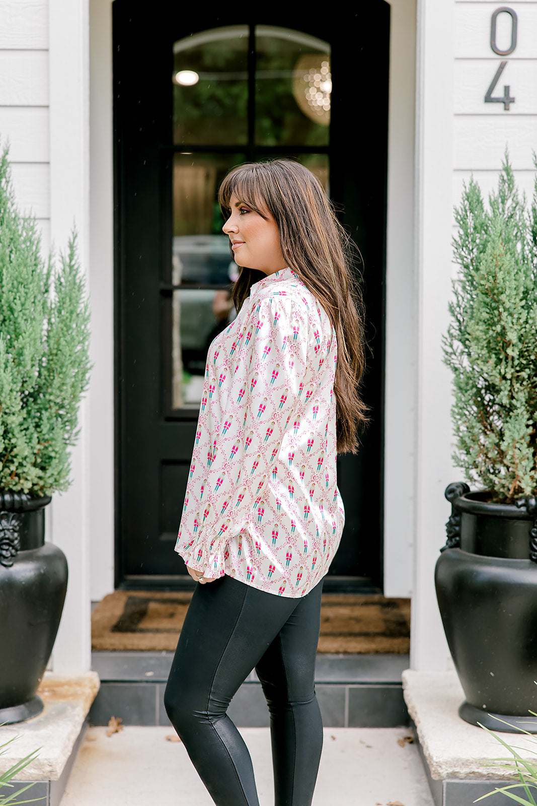 Woman with dark hair wearing a long-sleeve silky top with nutcracker graphics. Model paired this top with faux leather leggings.