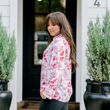 Woman with dark hair wearing a long-sleeve red & cream Santa toile graphics top. Model paired this top with leather pants.