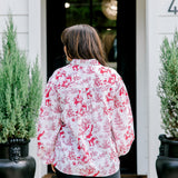 Woman with dark hair wearing a long-sleeve red & cream Santa toile graphics top. Model paired this top with leather pants.