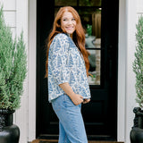 Woman with red hair wearing a quarter-sleeve top with blue Santa toile graphics and blue embroidery on shoulders and chest. Model paired this top with denim jeans.