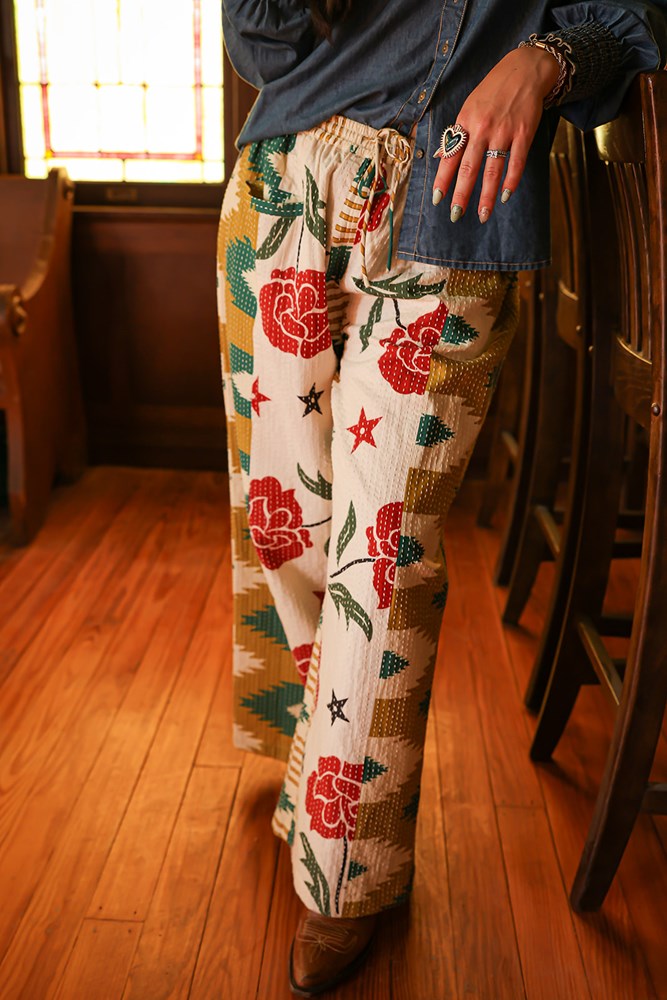 Woman with dark hair wearing the Pendleton Pants featuring stars embellishments, red rose graphics, and aztec print down side of pants.