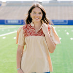 Woman facing forward wearing a short-sleeve orange shirt with burnt orange embroidery and dark-wash denim shorts.