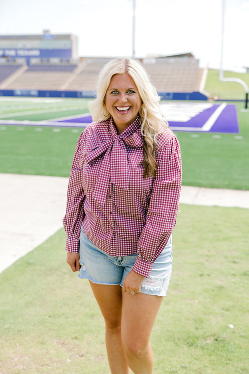 Woman with blonde hair wearing maroon gingham long-sleeve, tied in the front with light-wash denim shorts.