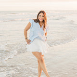 A woman with dark hair standing in front profile position wearing the Scarlett Top in a lifestyle scene. The focal point of the image is the top in its entirety. The model paired this top with a white skirt.