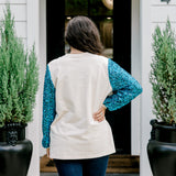 Woman with dark hair wearing a sweatshirt with turquoise sparkle sleeves & embroidery on front that says "Jesus Is The Reason". Model paired this top with dark-wash denim jeans.