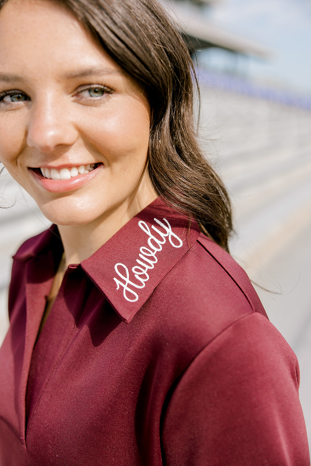 Woman with dark hair wearing a maroon dress with a close-up on howdy embroidery.