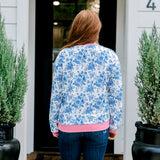 Woman with red hair wearing a blue floral sweatshirt with pink accents and "Merry Christmas" embroidered on front. Model paired this top with denim jeans.