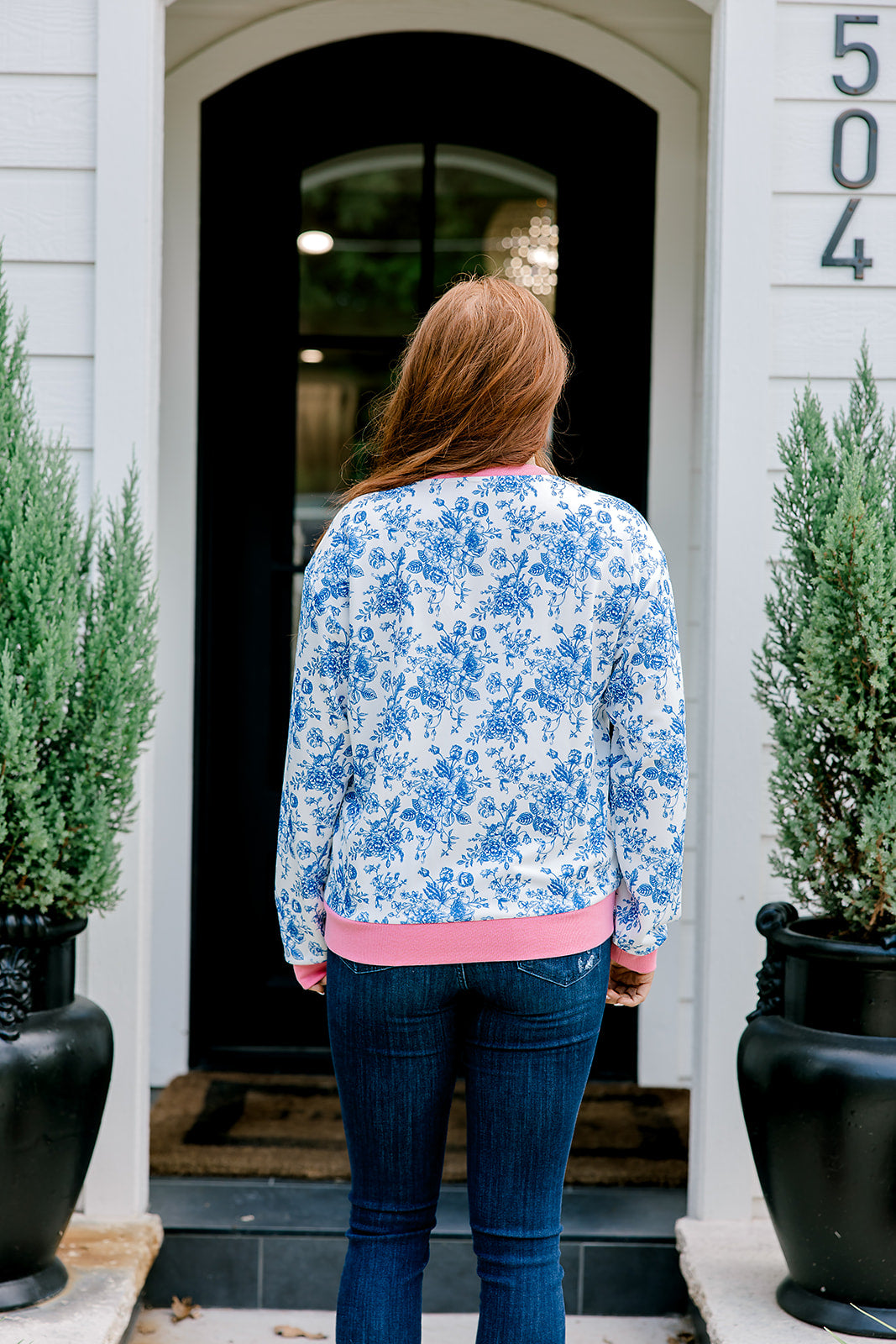 Woman with red hair wearing a blue floral sweatshirt with pink accents and "Merry Christmas" embroidered on front. Model paired this top with denim jeans.