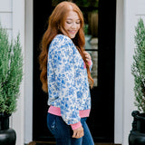 Woman with red hair wearing a blue floral sweatshirt with pink accents and "Merry Christmas" embroidered on front. Model paired this top with denim jeans.