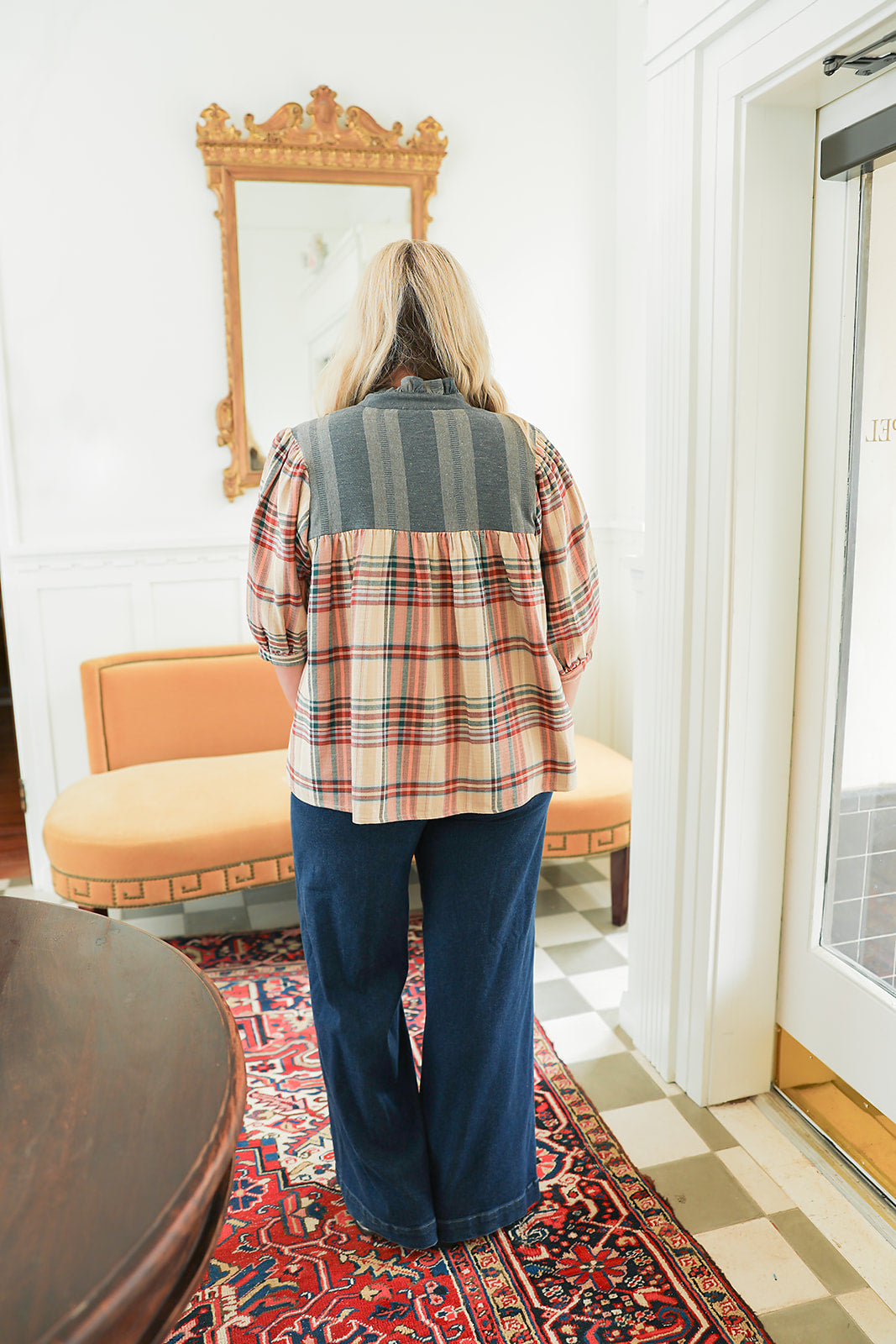 Woman with blonde hair wearing a quarter sleeve top with plaid patch-work paired with dark-wash denim jeans.