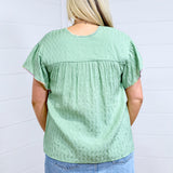 Woman with blonde hair standing in a back profile position wearing the Ada Top against a white background. The focal point of this image is the pleating on back of top as well as flowy sleeves. The model paired this top with a light-wash denim skirt. 
