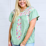 Woman with blonde hair standing in a front profile position wearing the Ada Top against a white background. The focal point of this image is the embroidery down the front, sides and chest as well as the intricate details around neckline. The model paired this top with a light-wash denim skirt. 
