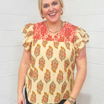 Woman with blonde hair standing in a front profile position wearing the Alura Top against a white background. The focal point of this image is the floral graphics and embroidery across chest of top. The model paired this top with dark-wash denim jeans. 