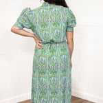 Woman with dark hair standing in a back profile position wearing the Amelia Dress against a white background. The focal point of this image is the pink, green, and orange floral graphics on the back and the puffy-cuffed sleeves.