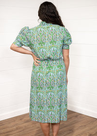 Woman with dark hair standing in a back profile position wearing the Amelia Dress against a white background. The focal point of this image is the pink, green, and orange floral graphics on the back and the puffy-cuffed sleeves.