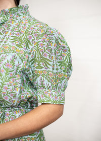 Woman with dark hair standing in a front profile position wearing the Amelia Dress against a white background. The focal point of this image is the floral detail in the sleeve, and detail on cuff. 