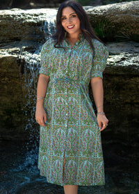 Woman with dark hair standing in a front profile position wearing the Amelia Dress in a lifestyle scene. The focal point of this image is the Amelia Dress against a water focused background. 