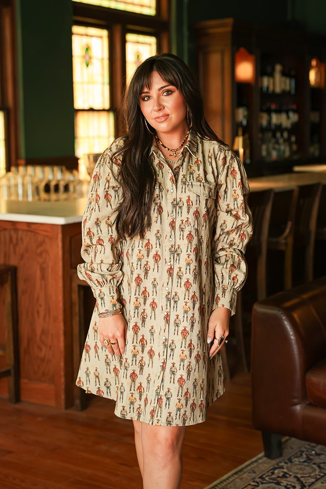 Woman with dark hair wearing a midi long-sleeve dress with cowboy graphics. Model paired this dress with brown and white booties. 