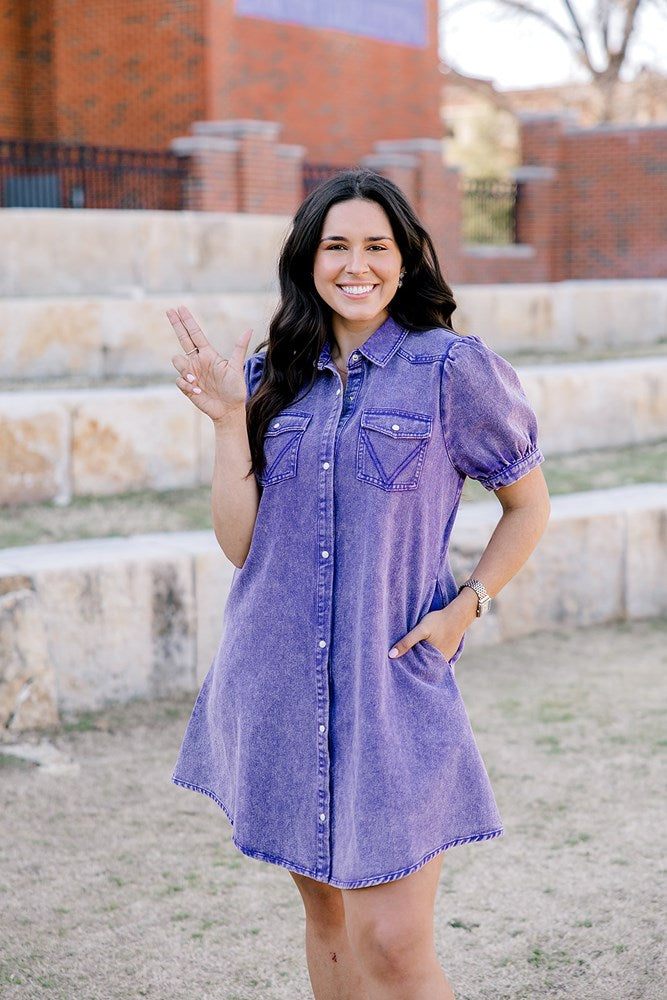 Woman with dark hair standing in a front profile position wearing the Annie Dress in a lifestyle scene. The focal point of this image is the pockets on front of dress, ruffles sleeves, pearl snaps, and length of dress. 