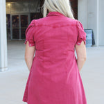 Woman with blonde hair wearing a maroon denim dress.