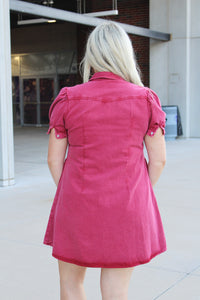 Woman with blonde hair wearing a maroon denim dress.