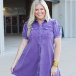 Woman with blonde hair standing in a front profile position wearing the Annie Dress at a football stadium. The focal point of this image is length of dress, and pearl snap buttons down the front.  