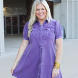 Woman with blonde hair standing in a front profile position wearing the Annie Dress at a football stadium. The focal point of this image is length of dress, and pearl snap buttons down the front.  