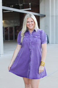 Woman with blonde hair standing in a front profile position wearing the Annie Dress at a football stadium. The focal point of this image is length of dress, and pearl snap buttons down the front.  
