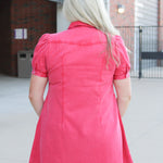 Woman with blonde hair standing in a back profile position wearing a midi red denim dress.