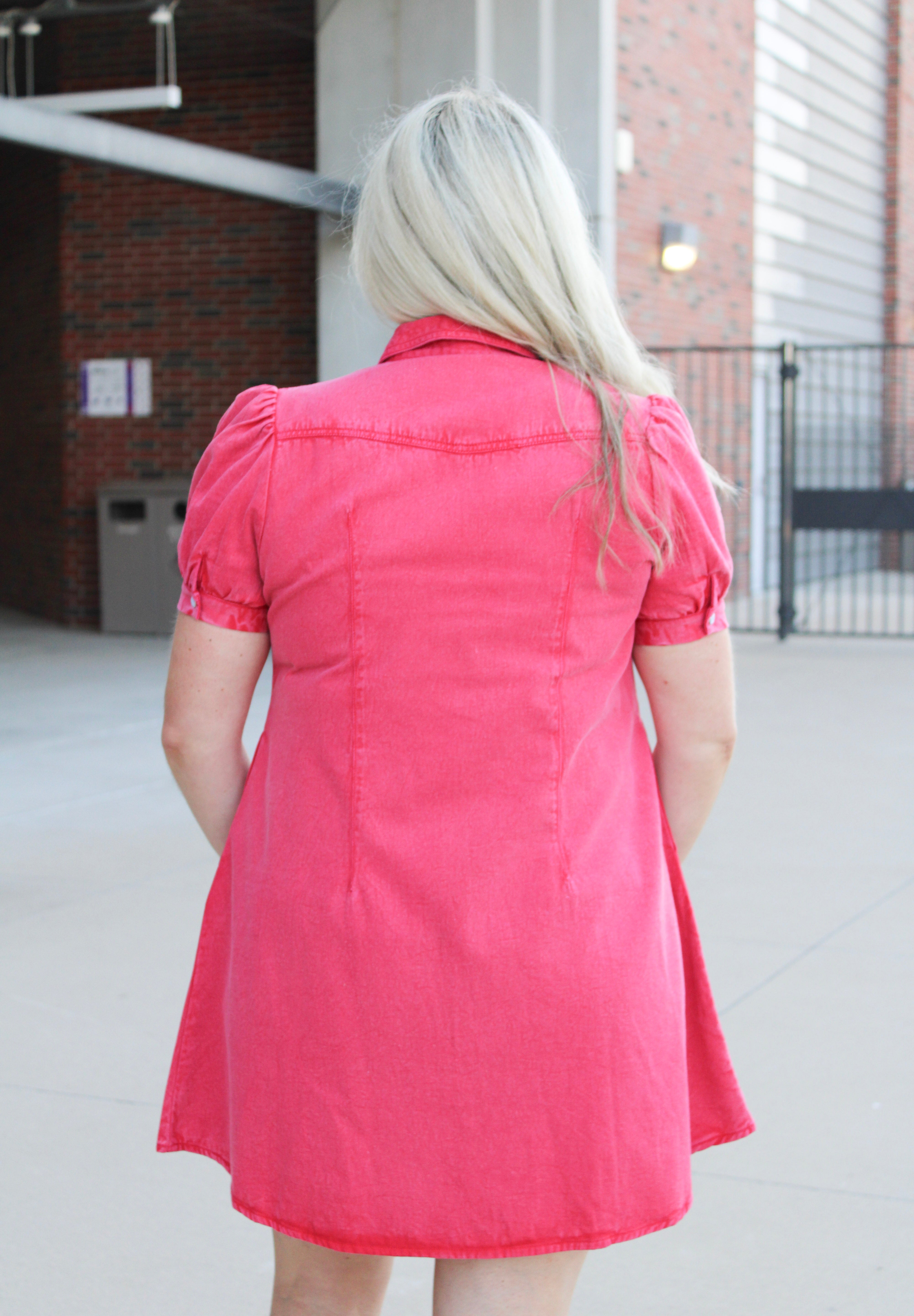 Woman with blonde hair standing in a back profile position wearing a midi red denim dress.