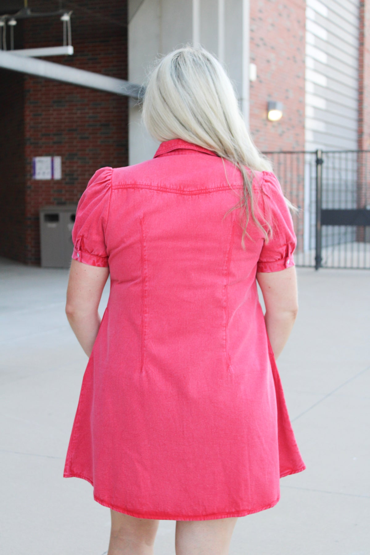 Woman with blonde hair standing in a back profile position wearing a midi red denim dress.