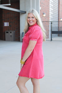 Woman with blonde hair standing in a side profile position wearing a midi red denim dress. 