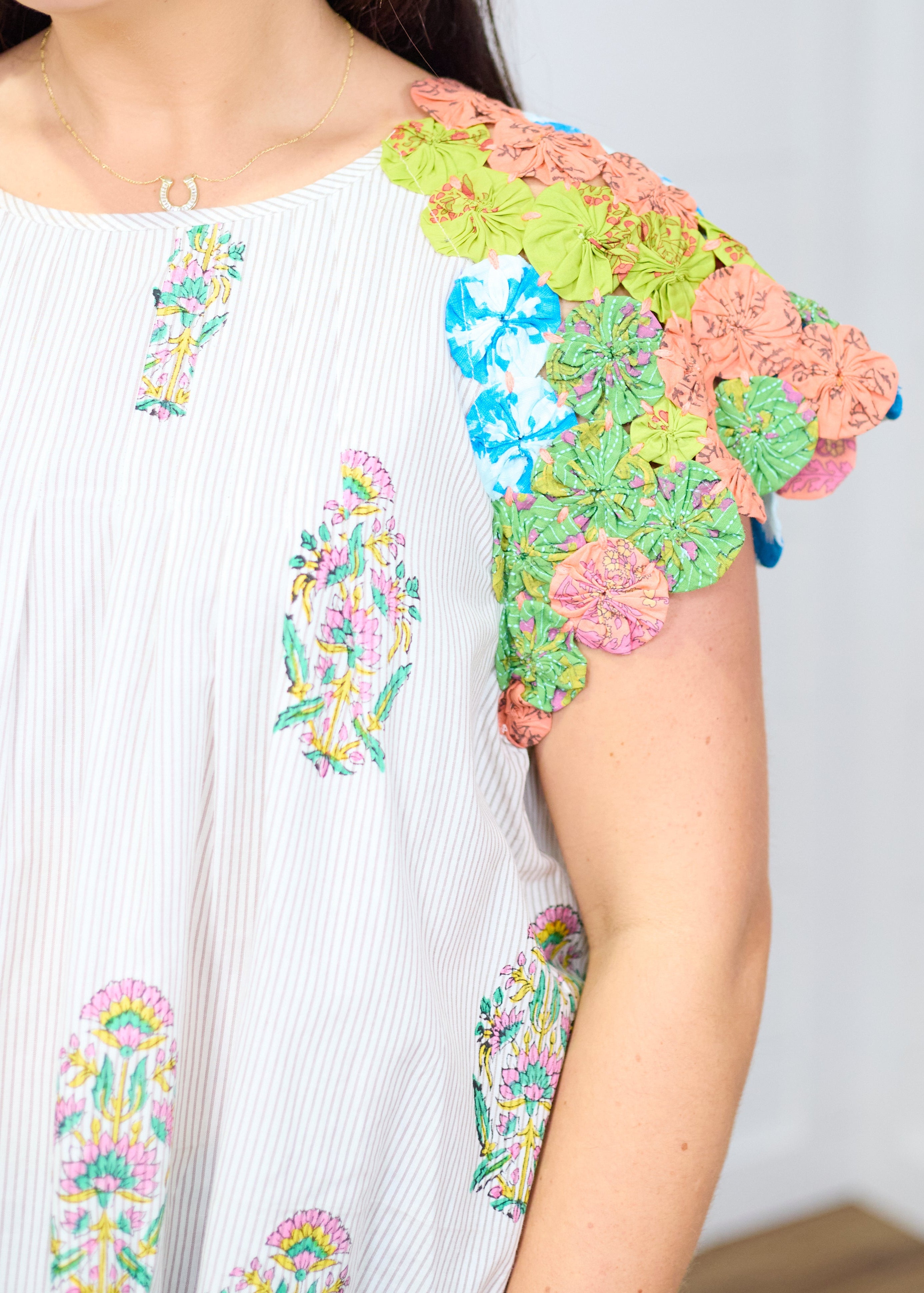Woman with dark hair standing against a white background with a deep focal focus on sleeve of top. Top shows in depth pinwheel fabric on sleeve to give a better perception of detail. 