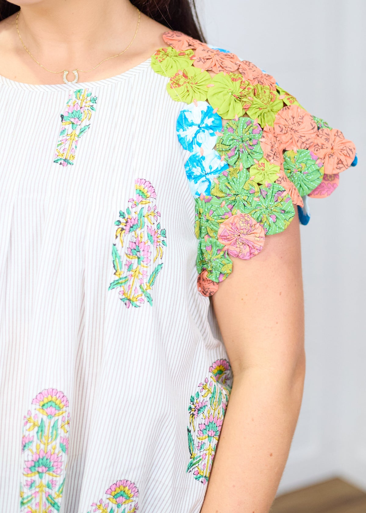 Woman with dark hair standing against a white background with a deep focal focus on sleeve of top. Top shows in depth pinwheel fabric on sleeve to give a better perception of detail. 