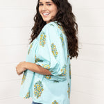 Woman with dark hair standing in a side profile position wearing the Ava Top against a white background. The focal point of this image is to see puffy sleeve length. The model paired this top with dark-wash denim jeans. 