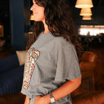 Woman with dark hair standing in a side profile position wearing the Basic Tee in  a lifestyle scene. The focal point of this image is the side profile of the tee and sneak peek of embroidery on the front. The model paired this top with light-wash denim jeans. 