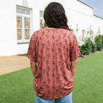 Woman with dark hair standing in a back profile position wearing the Basic Tee in a lifestyle scene. The focal point of this image is the cowgirl graphics on tee. The model paired this tee with light-wash denim jeans.