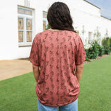 Woman with dark hair standing in a back profile position wearing the Basic Tee in a lifestyle scene. The focal point of this image is the cowgirl graphics on tee. The model paired this tee with light-wash denim jeans.