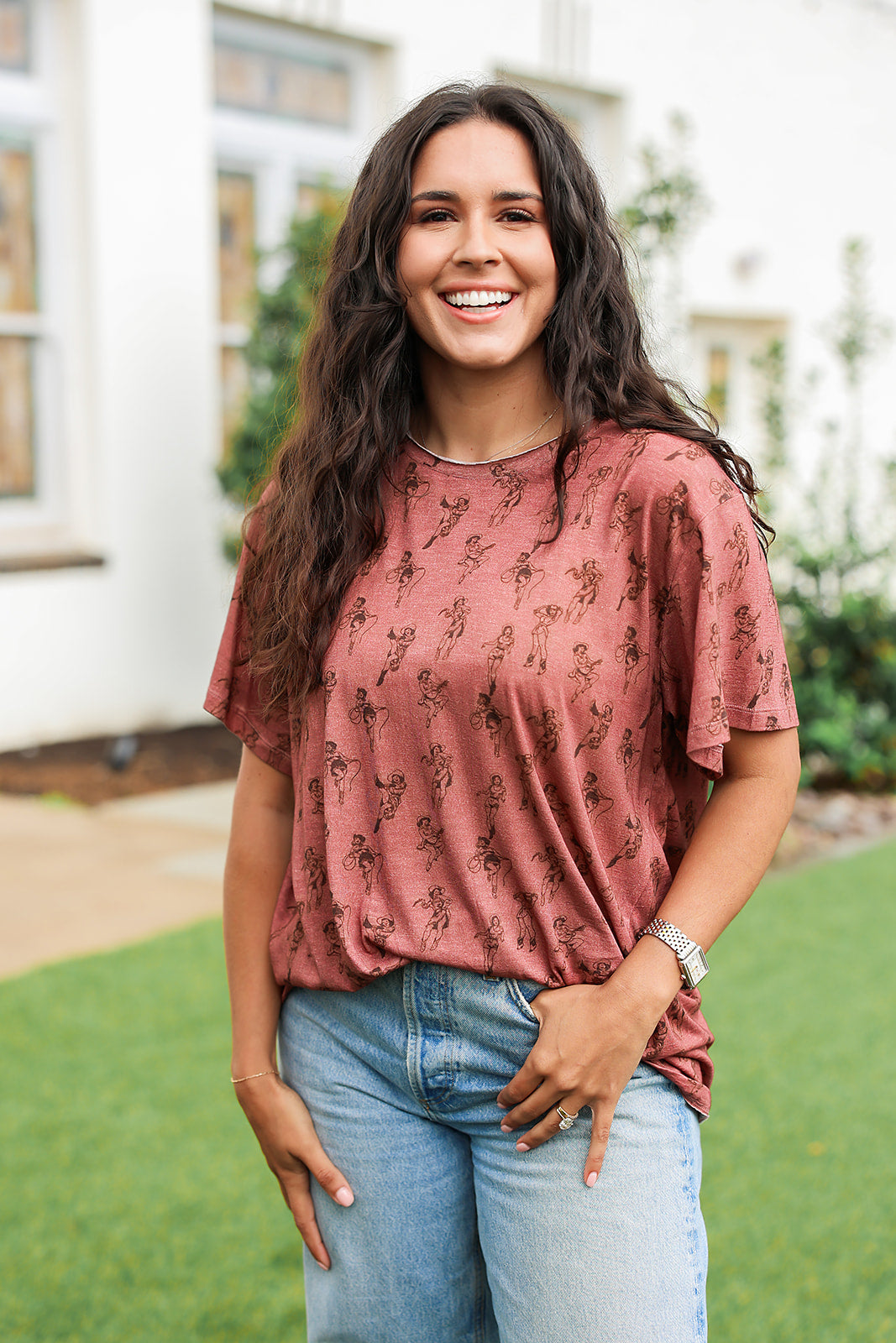 Woman with dark hair standing in a front profile position wearing the Basic Tee in a lifestyle scene. The focal point of this image is the graphics on front of tee. 