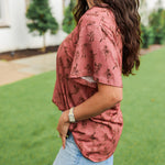 Woman with dark hair standing in a side profile position wearing the Basic Tee in a lifestyle scene. The focal point of this image is the side profile of tee with graphics. The model paired this top with light-wash denim jeans. 
