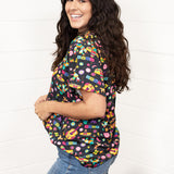 Woman with dark hair standing in a side profile position wearing the Basic Tee against a white background. The focal point of this image is the graphics along side of tee as well as shoulder length. The model paired this top with dark-wash denim jeans. 