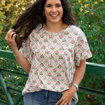 Woman with dark hair standing in a front profile position wearing the Basic Tee in a lifestyle scene. The focal point of this image is the pink and green floral graphics against heavy greenery background. The model paired this top with dark-wash denim jeans. 