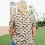Woman with blonde hair standing in a back profile position wearing the Basic Tee in a lifestyle scene. The focal point of this image is the western cowboy hats on a cream colored tee. The model paired this tee with dark-wash denim jeans. 
