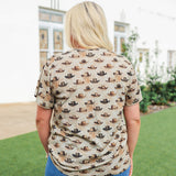 Woman with blonde hair standing in a back profile position wearing the Basic Tee in a lifestyle scene. The focal point of this image is the western cowboy hats on a cream colored tee. The model paired this tee with dark-wash denim jeans. 