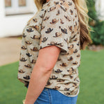 Woman with blonde hair standing in a side profile position wearing the Basic Tee in a lifestyle scene. The focal point of this image is the side profile of the tee. The model paired this tee with dark-wash denim jeans. 