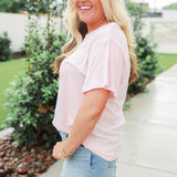Woman with blonde hair standing in a side profile position wearing the Basic Tee in a lifestyle scene. The focal point of this image is the side profile of tee. The model paired this tee with light-wash denim jeans. 