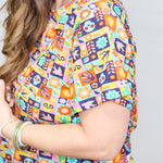 Woman with dark hair standing in a side profile position wearing the Basic Tee against a white background. The focal point of this image is the graphics on top (sugar scull, cacti, bird, etc...). 