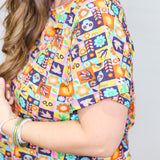 Woman with dark hair standing in a side profile position wearing the Basic Tee against a white background. The focal point of this image is the graphics on top (sugar scull, cacti, bird, etc...). 
