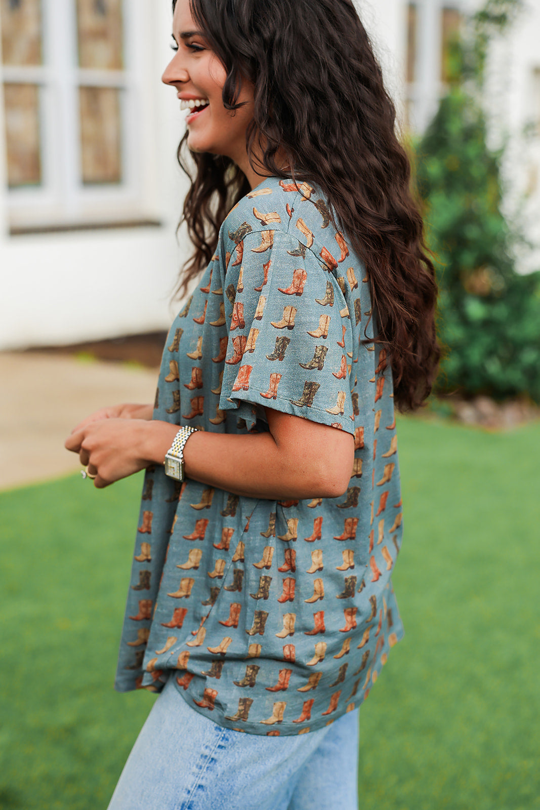 Woman with dark hair standing in a side profile position wearing the Basic Tee in a lifestyle scene. The model paired this top with light-wash denim jeans.